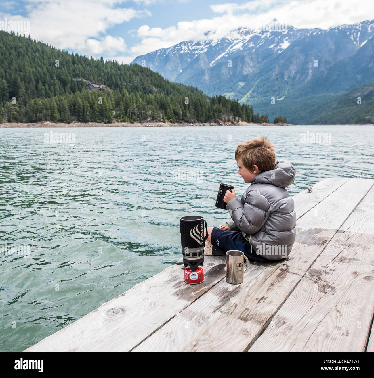 A boy sits on a dock drinking tea on Ross Lake in Washington's North Cascades National Park Stock Photo