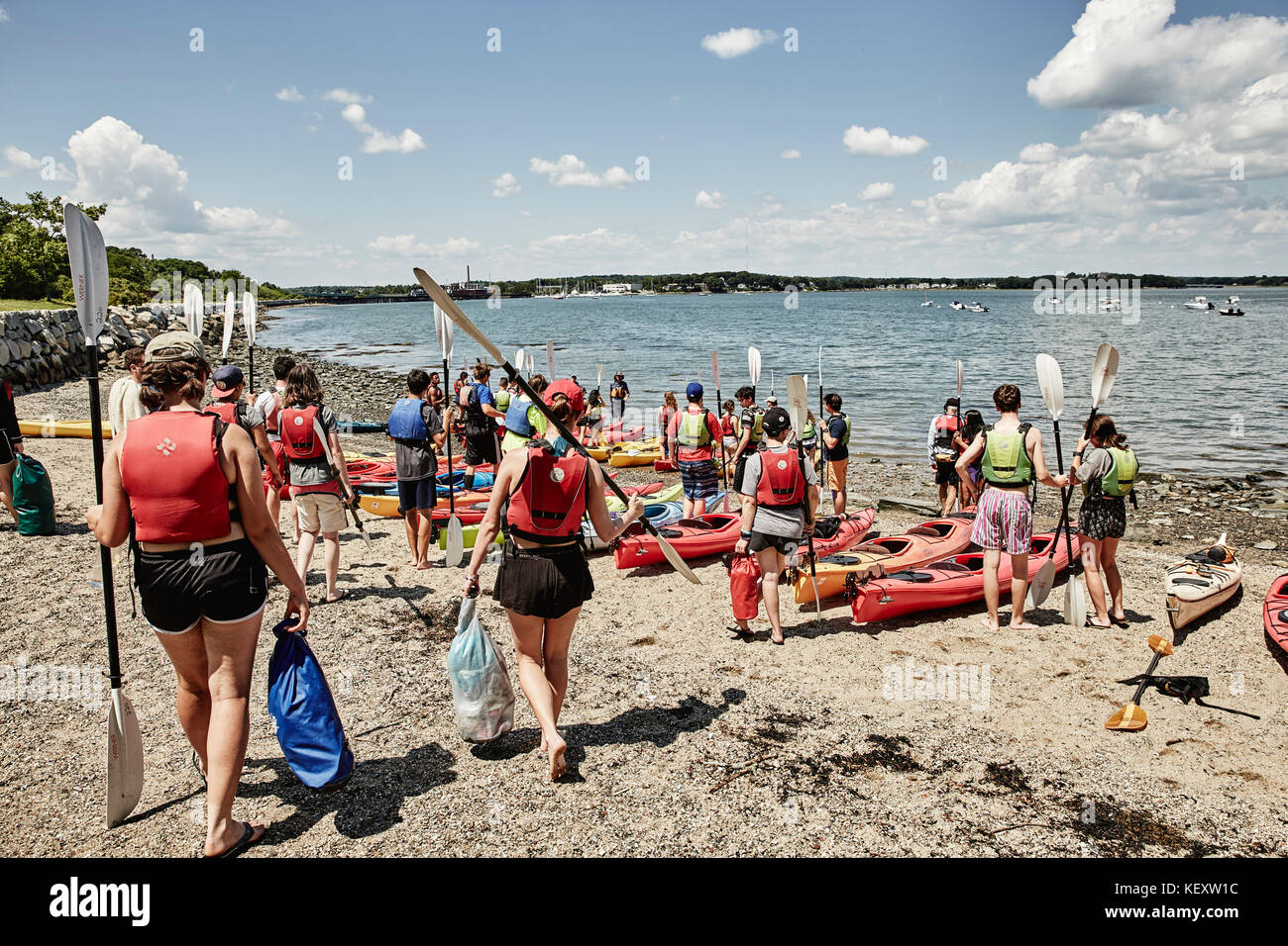 Group of people walking and standing with paddles beside kayaks lying on sea coast, Portland, Maine, USA Stock Photo
