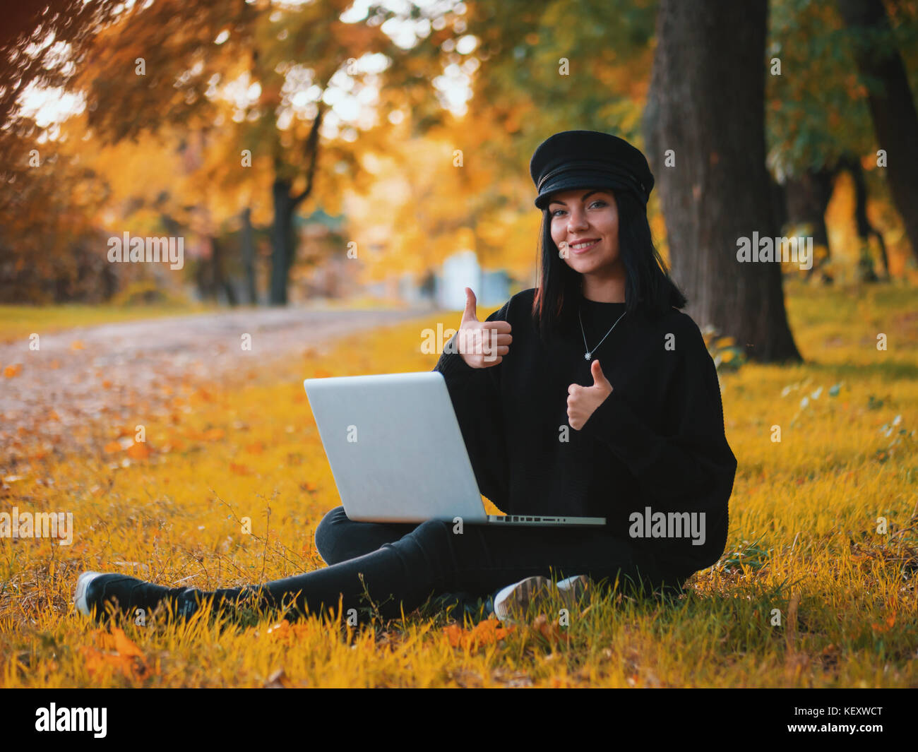 Young woman using laptop outdoor sitting on yellow grass and smiling ...