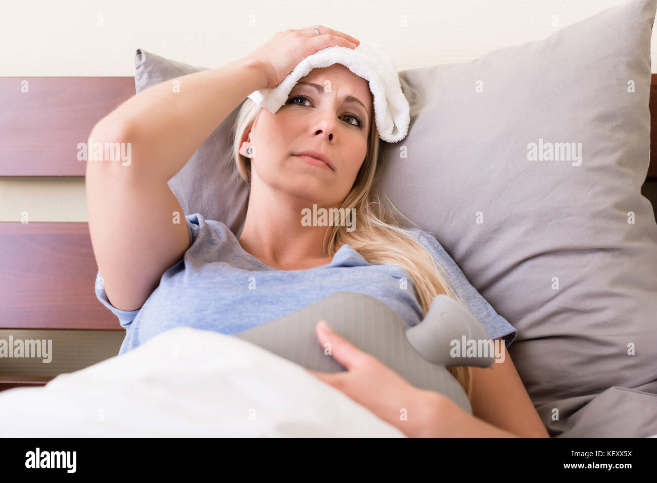 Young sick woman with fever lying in bed Stock Photo