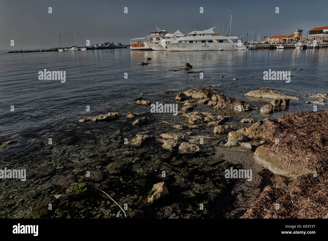 Rocks on the shore and moored pleasure boat in Paphos harbour in the mediterranean sea, Cyprus, europe Stock Photo