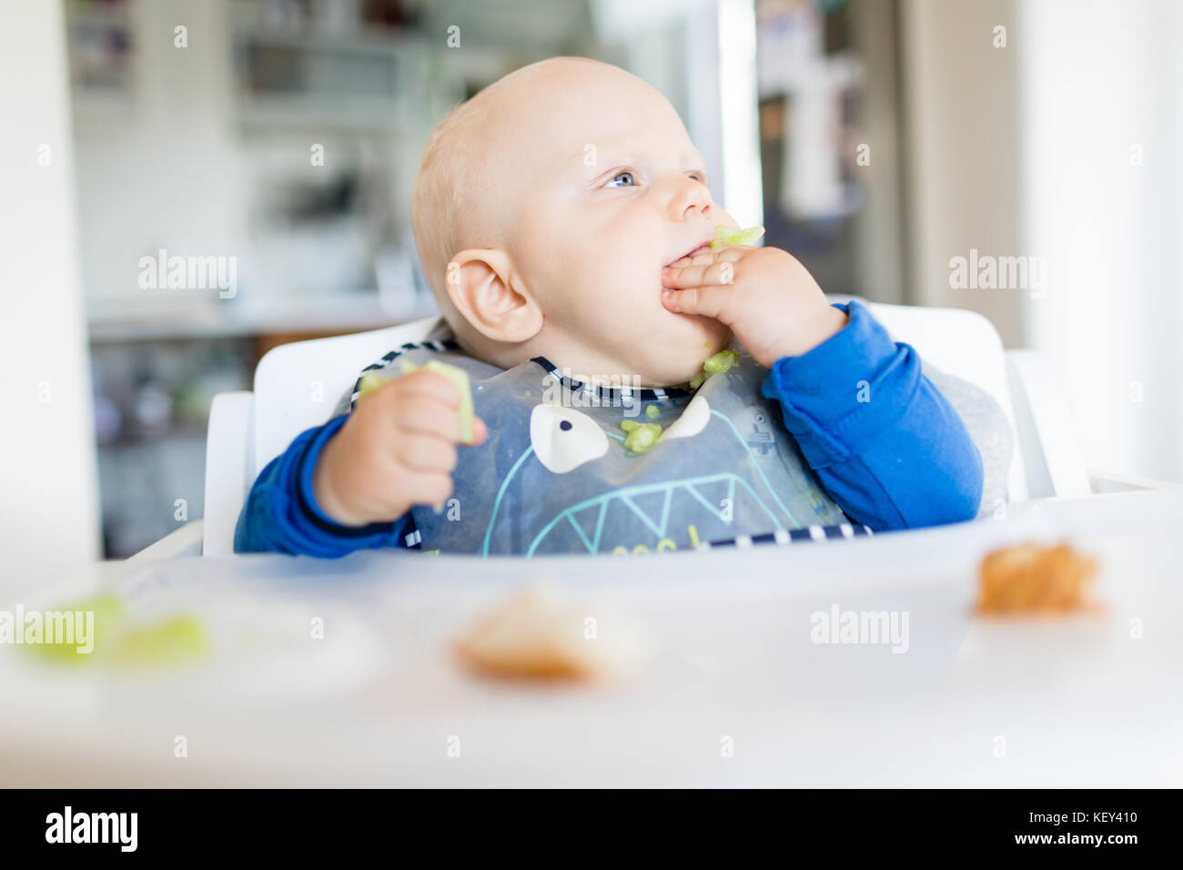 Baby boy eating bread and cucumber with BLW method, baby led weaning