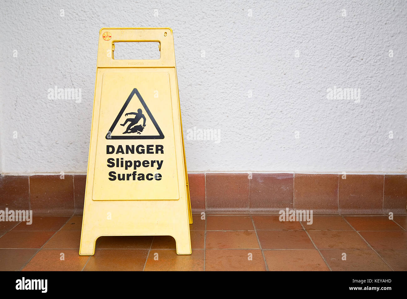 Yellow Danger Slippery Surface Sign On Tiled Floor On The Left