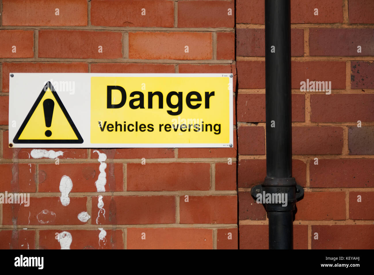 Danger vehicles reversing sign on red brick wall on the right hand side of the image Stock Photo