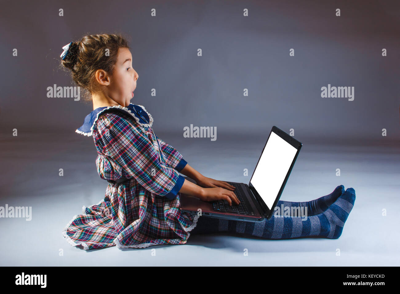 Girl child in a dress on a gray background looking computer Stock Photo ...