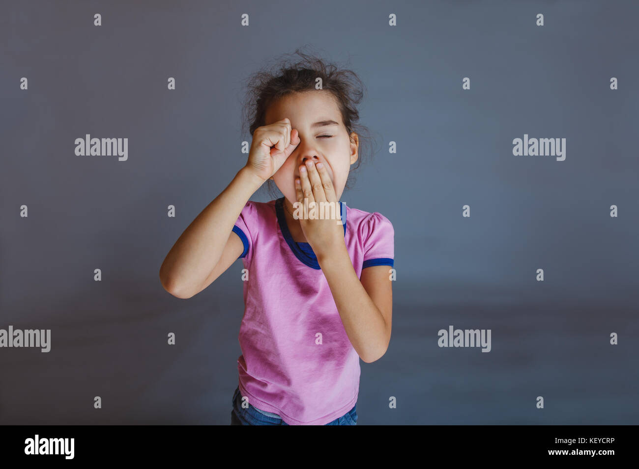 girl yawns t hand over his eyes on a gray background Stock Photo