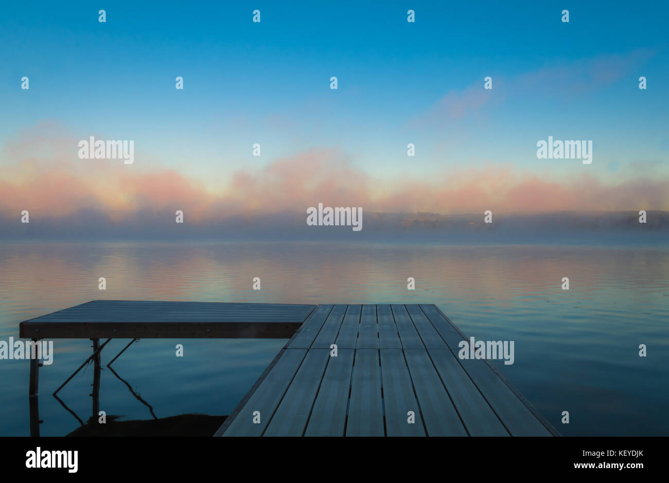 A dock overlooks a calm lake as the morning fog lifts in early autumn