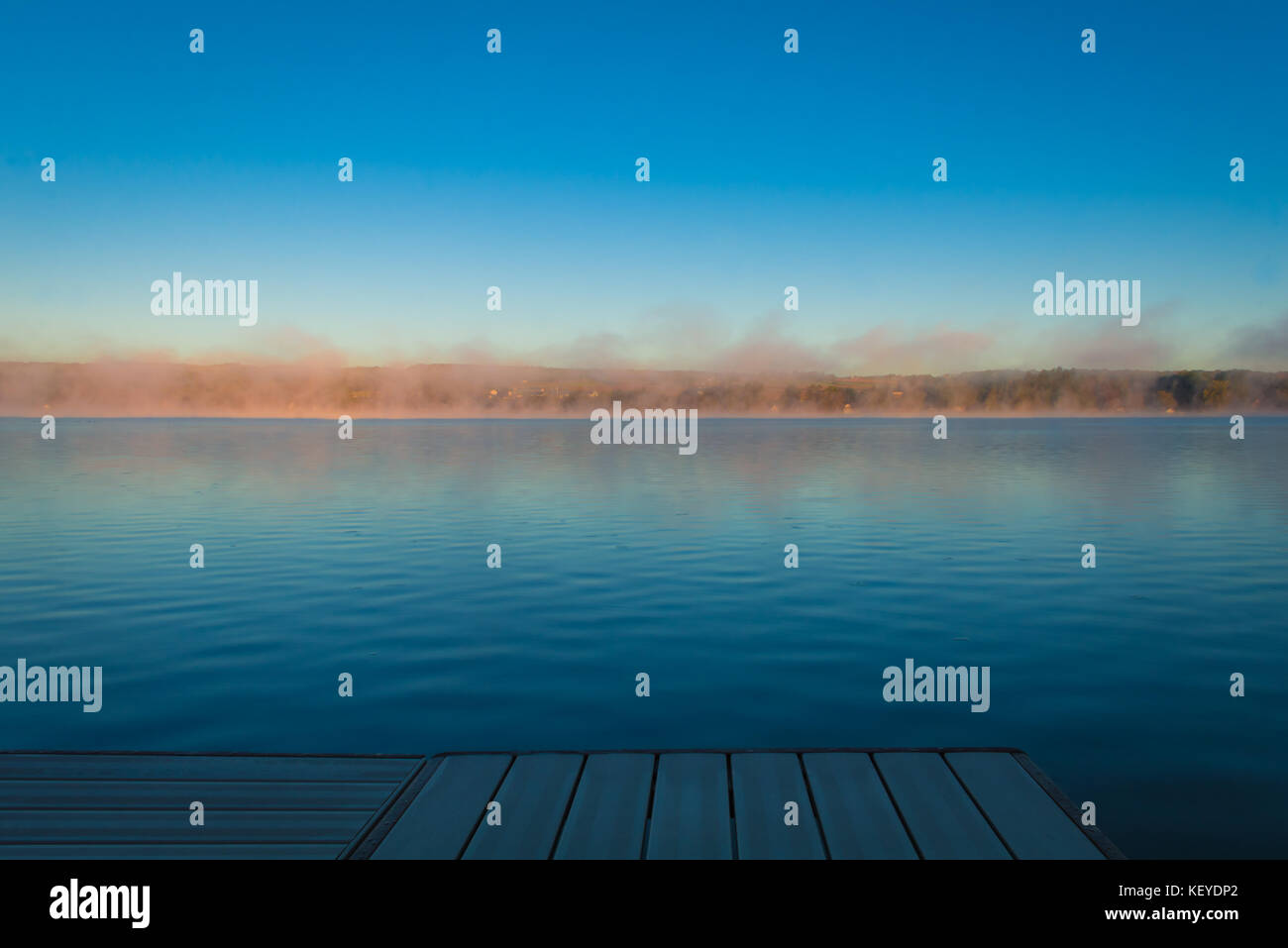 A dock overlooks a calm lake as the morning fog lifts in early autumn