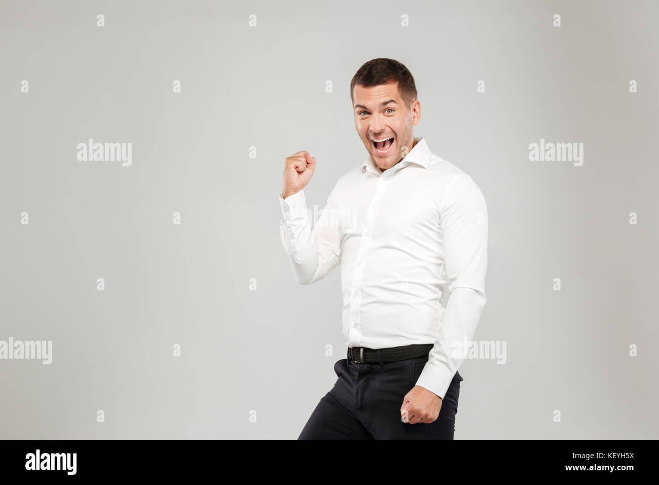 Excited screaming young man dressed in white shirt isolated over grey ...