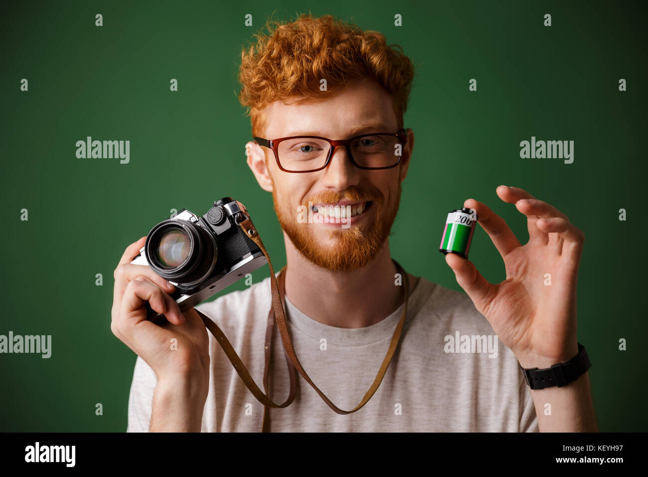 Close-up shot of young readhead bearded hipster holding retro photocamera and camera roll, over green background Stock Photo