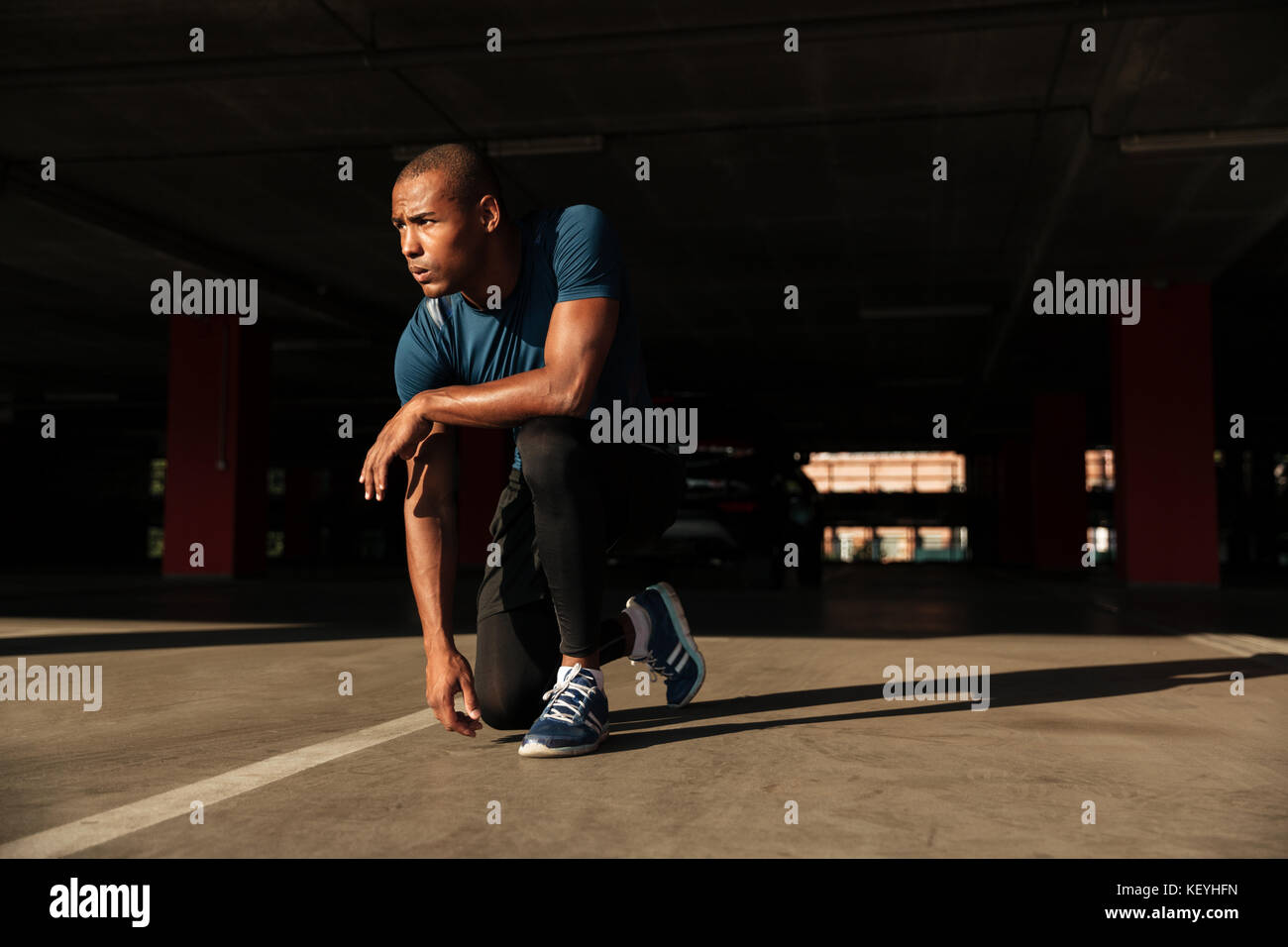 Portrait of a healthy african sportsman sitting on his knee and resting indoors Stock Photo