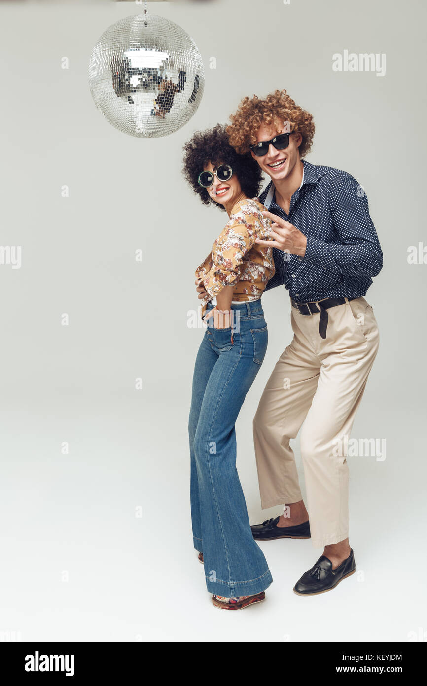 Picture of young emotional happy retro loving couple standing and posing isolated. Looking camera dancing near disco ball. Stock Photo