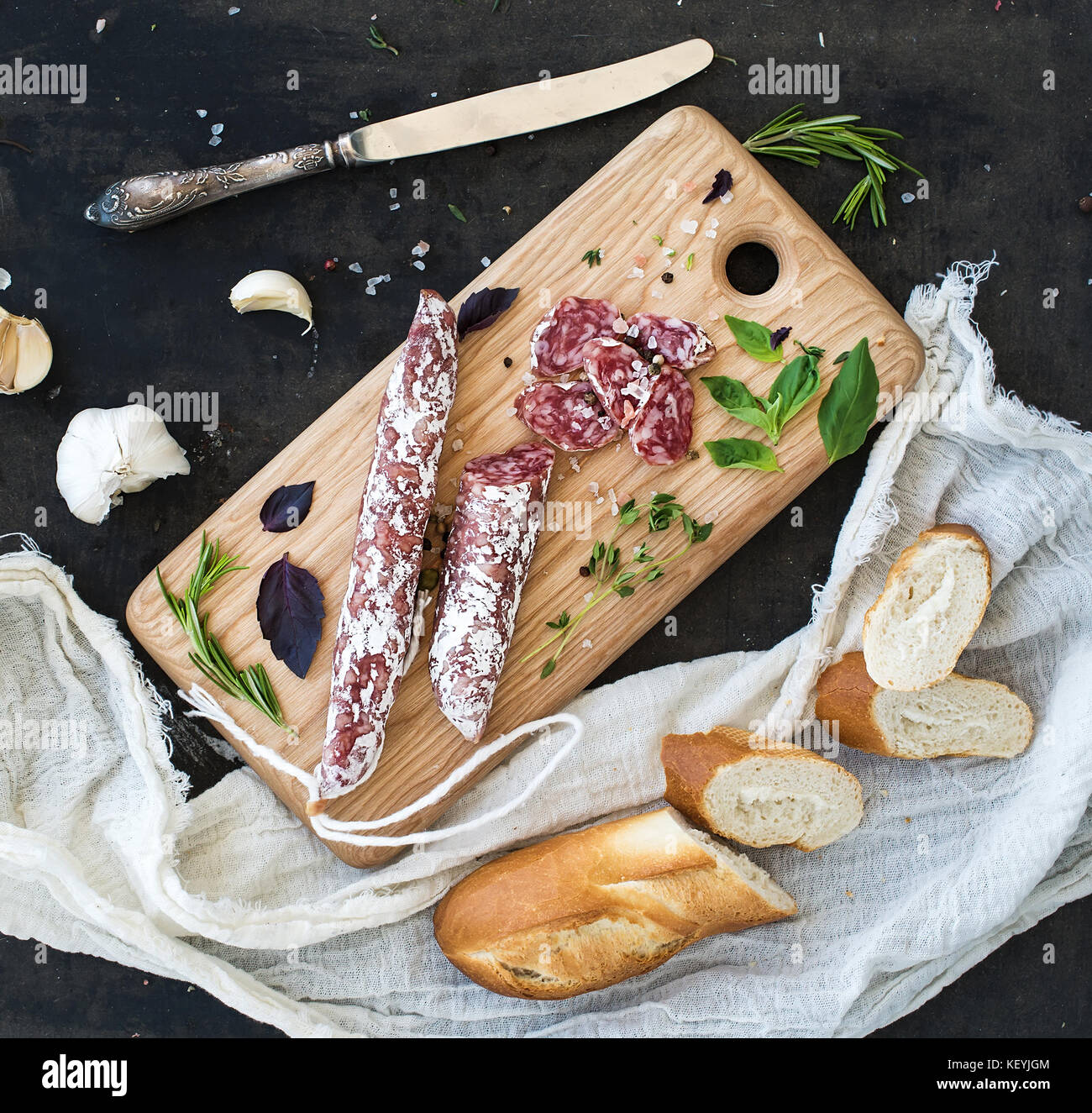 Meat gourmet snack. Salami, garlic, baguette and herbs on rustic wooden ...