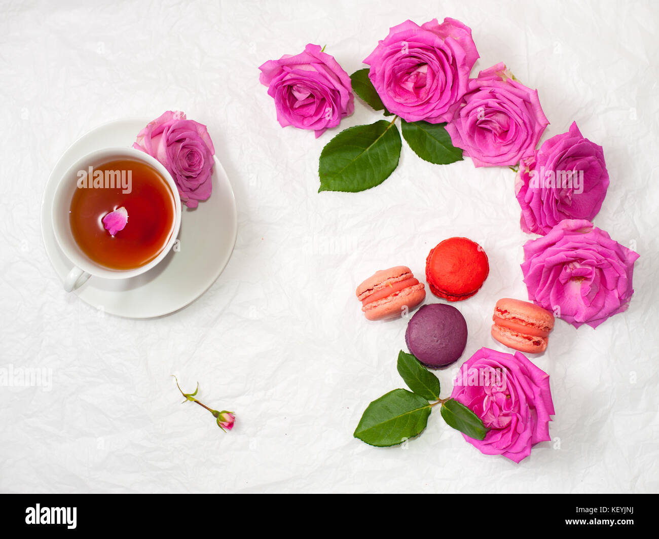 Flatlay of a cup of tea with rose petals, macarons and pink roses