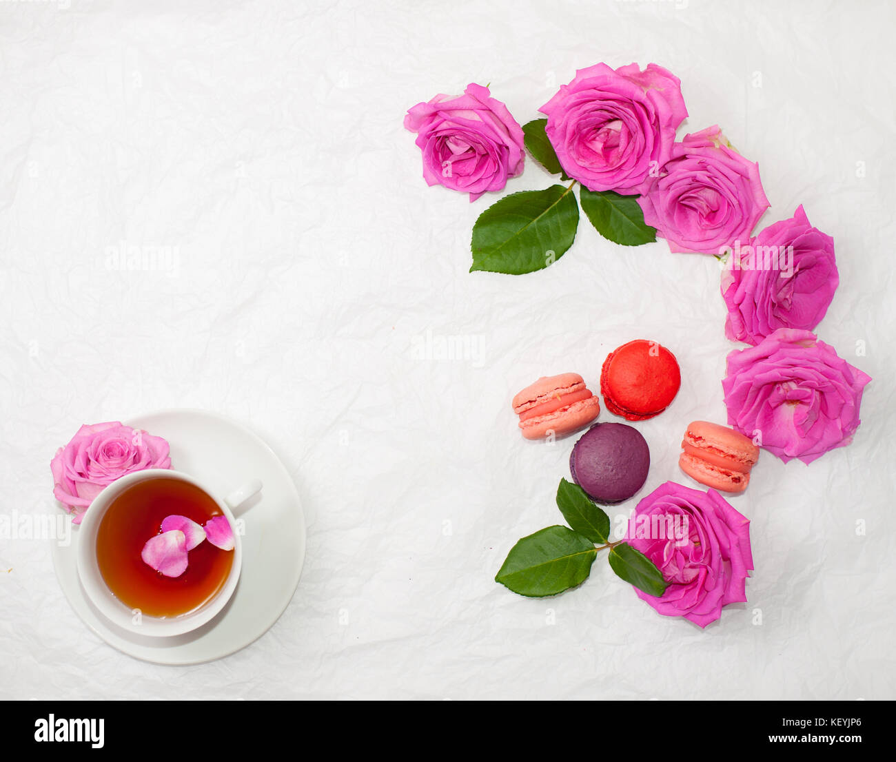Flatlay of a cup of tea with rose petals, macarons and pink roses
