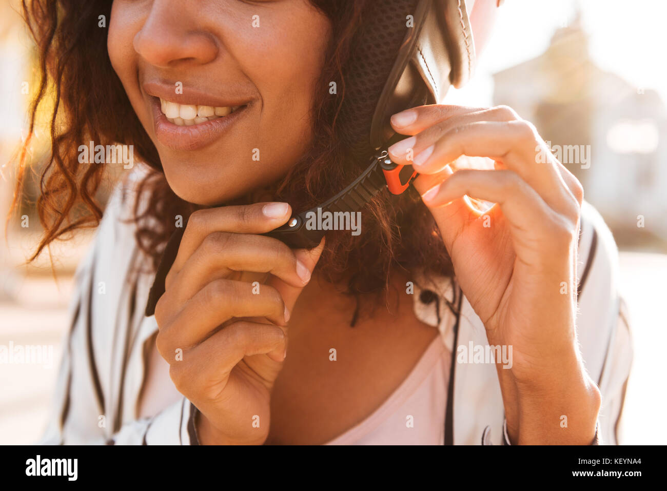 Cropped picture of happy african woman fastens her moto halmet outdoors Stock Photo