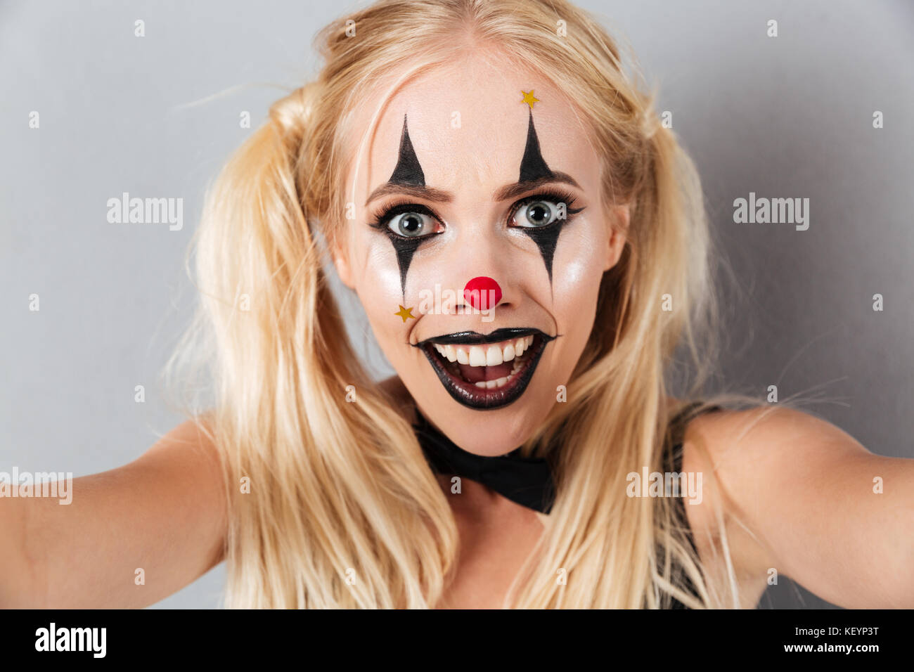 Close up portrait of an excited blonde woman in bright halloween clown  make-up taking a selfie isolated over gray background Stock Photo - Alamy