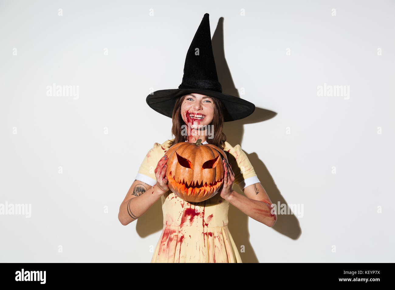 Laughing mad woman in halloween costume holding curved pumpkin and looking  at the camera over white background Stock Photo - Alamy