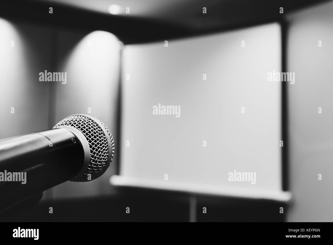 microphone ready to use in the podium and the projector screen on the back of the meeting room for the press conference. selective focus. black and wh Stock Photo