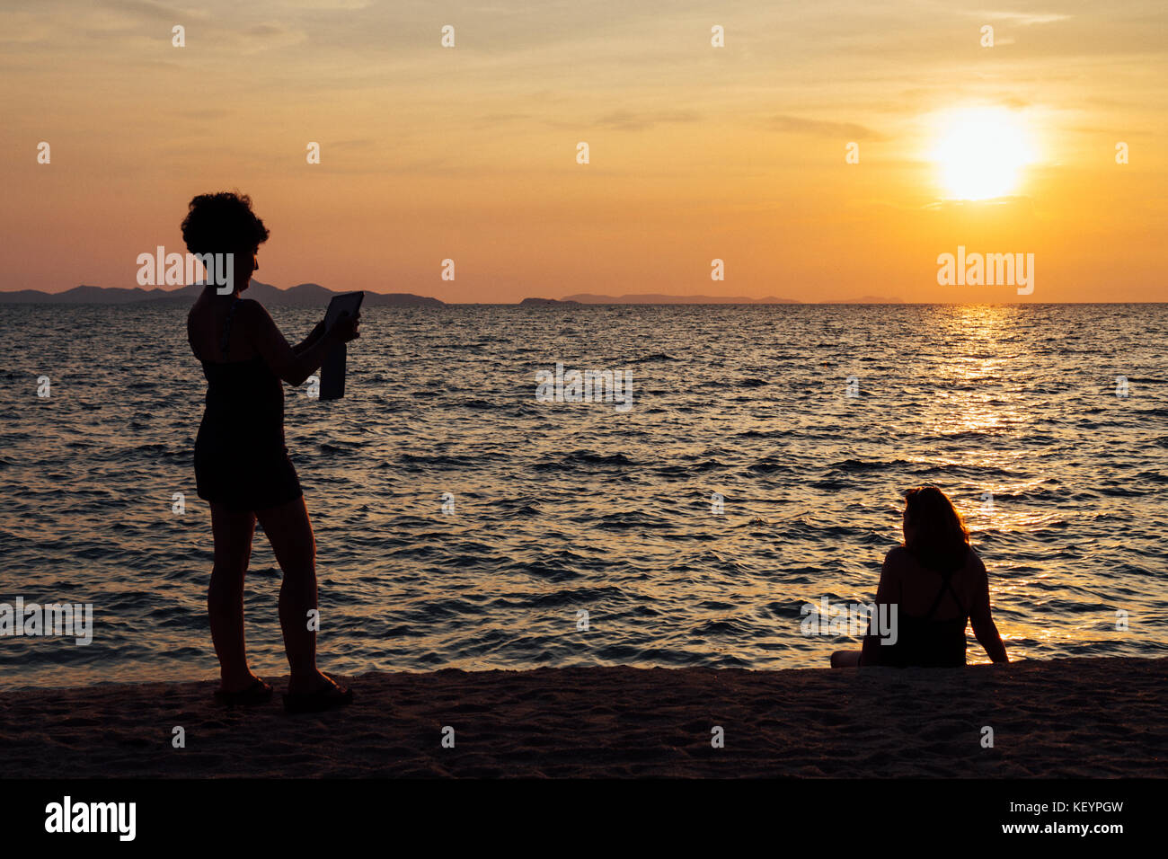 Woman taking a picture on the beach at sunset hi-res stock ...