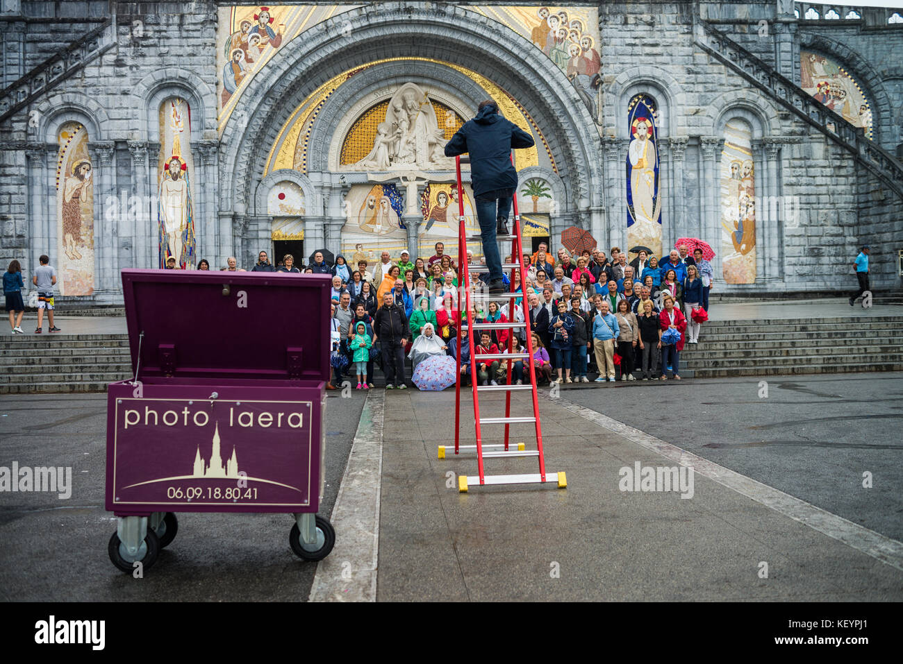 photographer taking pictures of group photo of tourists in front of the cathedral in Lourdes, France, Europe. Stock Photo