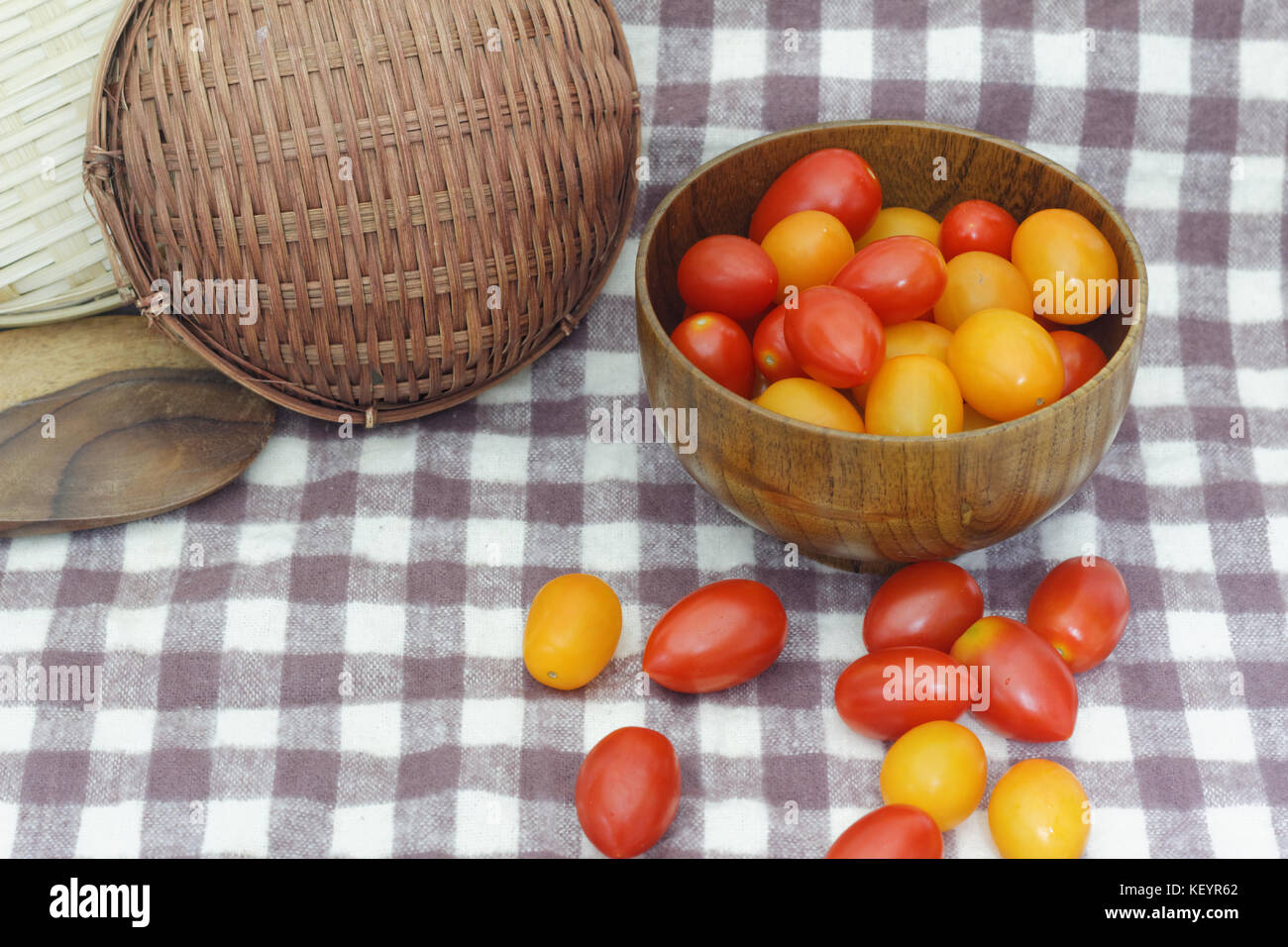 Small red cherry tomatoes spill out of a wicker basket on an old wooden ...
