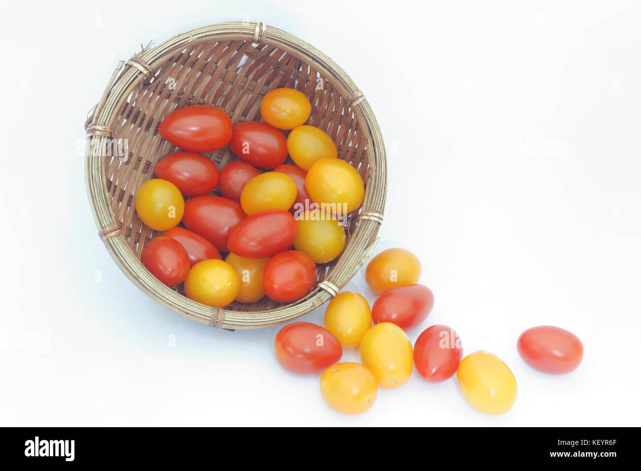 Small red and yellow cherry tomatoes spill out of a wicker basket on ...