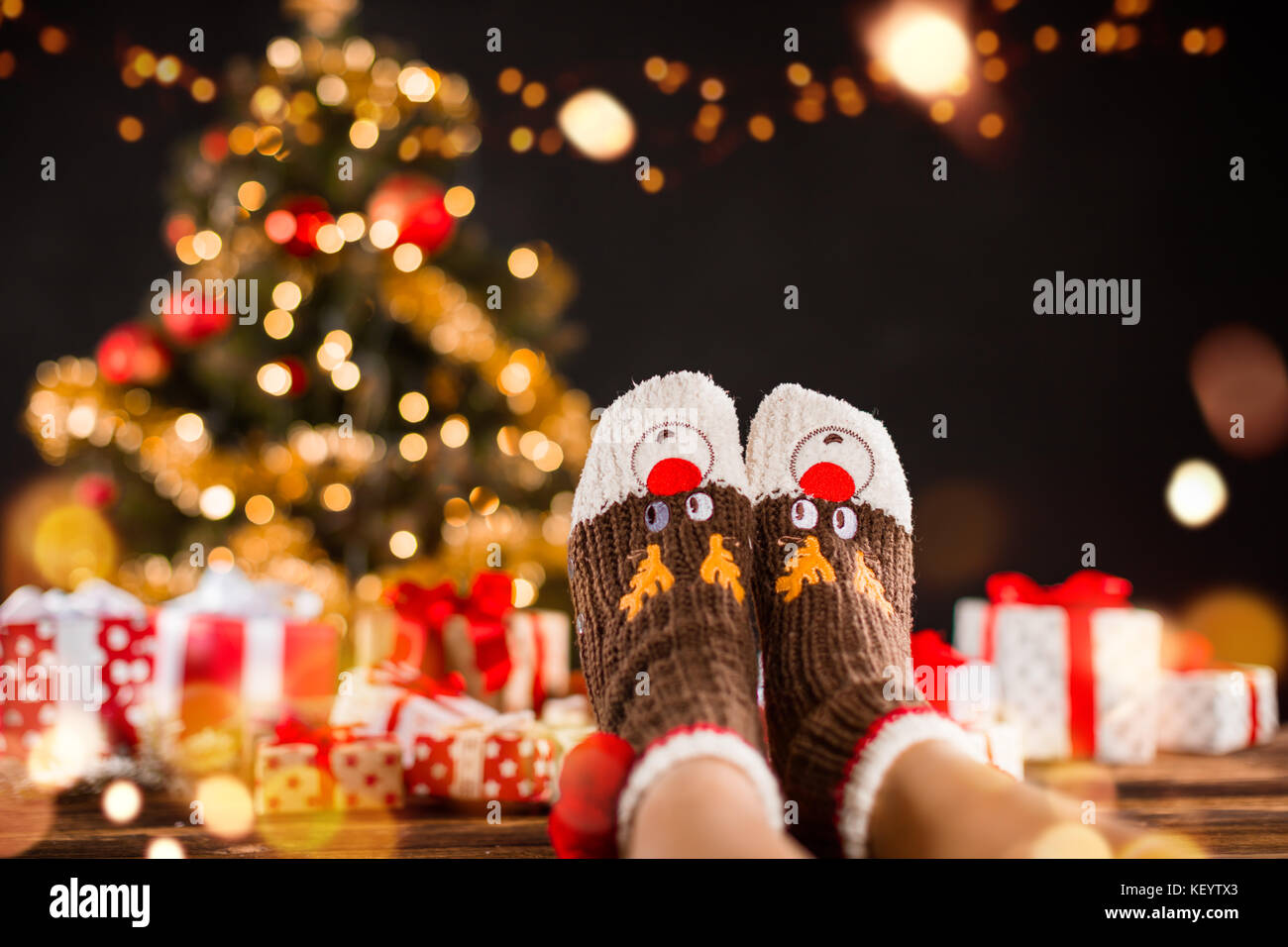 Detail of woman legs with knitted socks, Christmas tree with gifts on ...