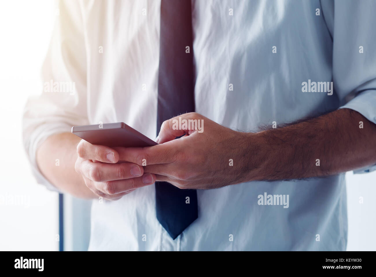 Business SMS message. Businessman using mobile phone to send bulk text messages to a whole business team. Stock Photo
