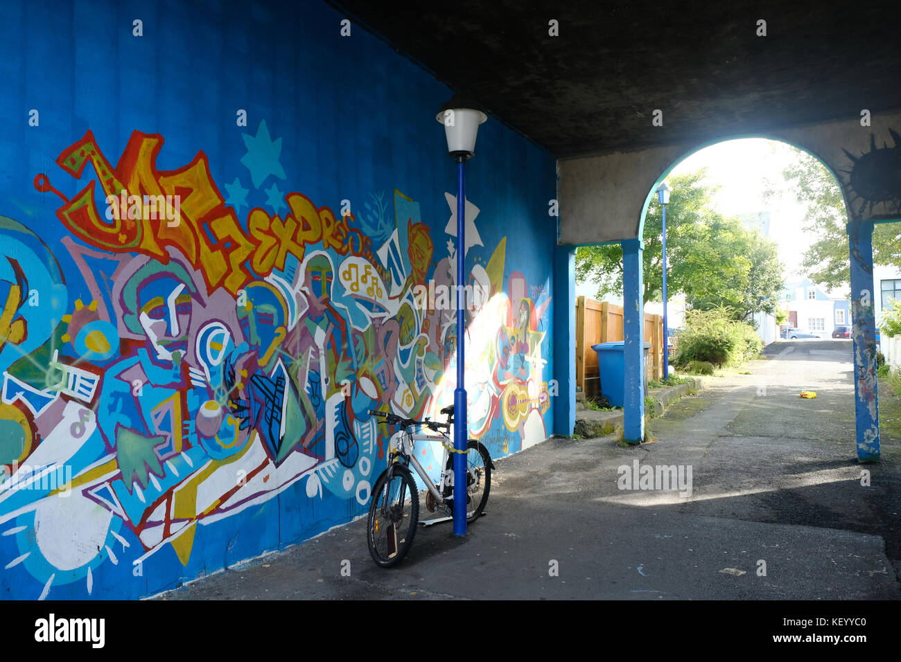 Bike leaning against blue lamppost and archway with graffiti on bright wall in old harbour area of Reykjavik capital city, Iceland Stock Photo