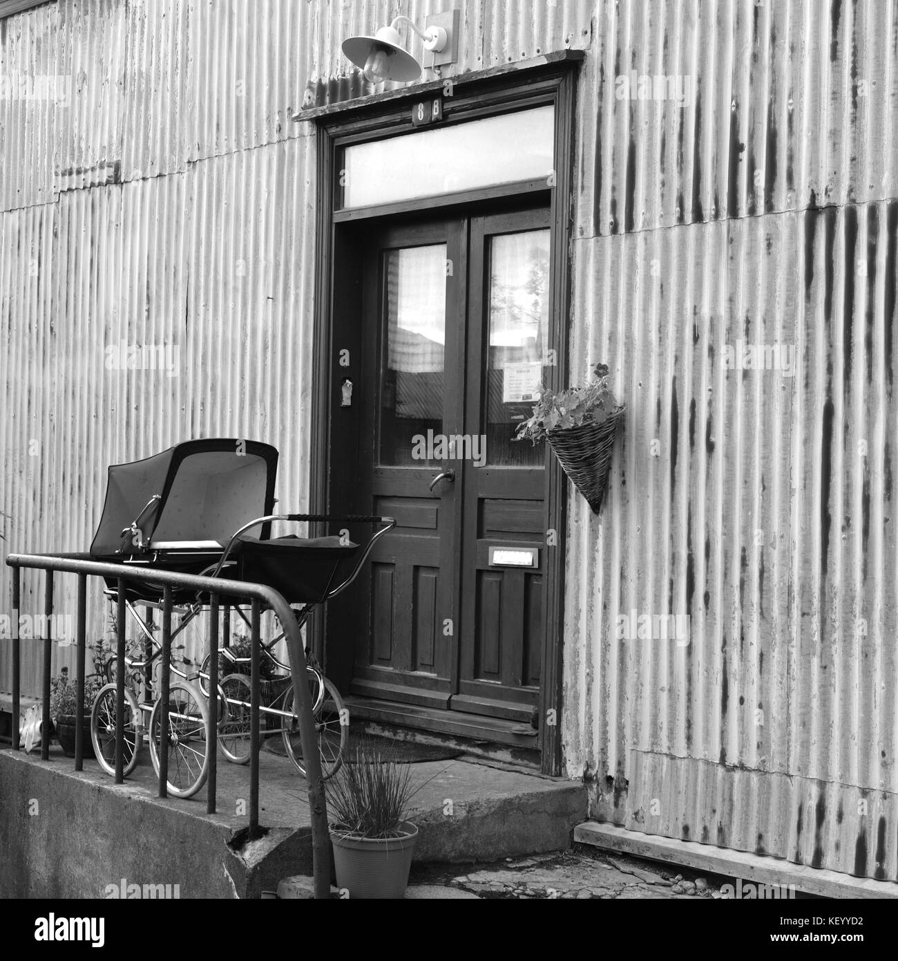 Old style vintage baby pram on front porch outside door of old house in black and white monochrome archival style square image, Reykjavik, Iceland Stock Photo