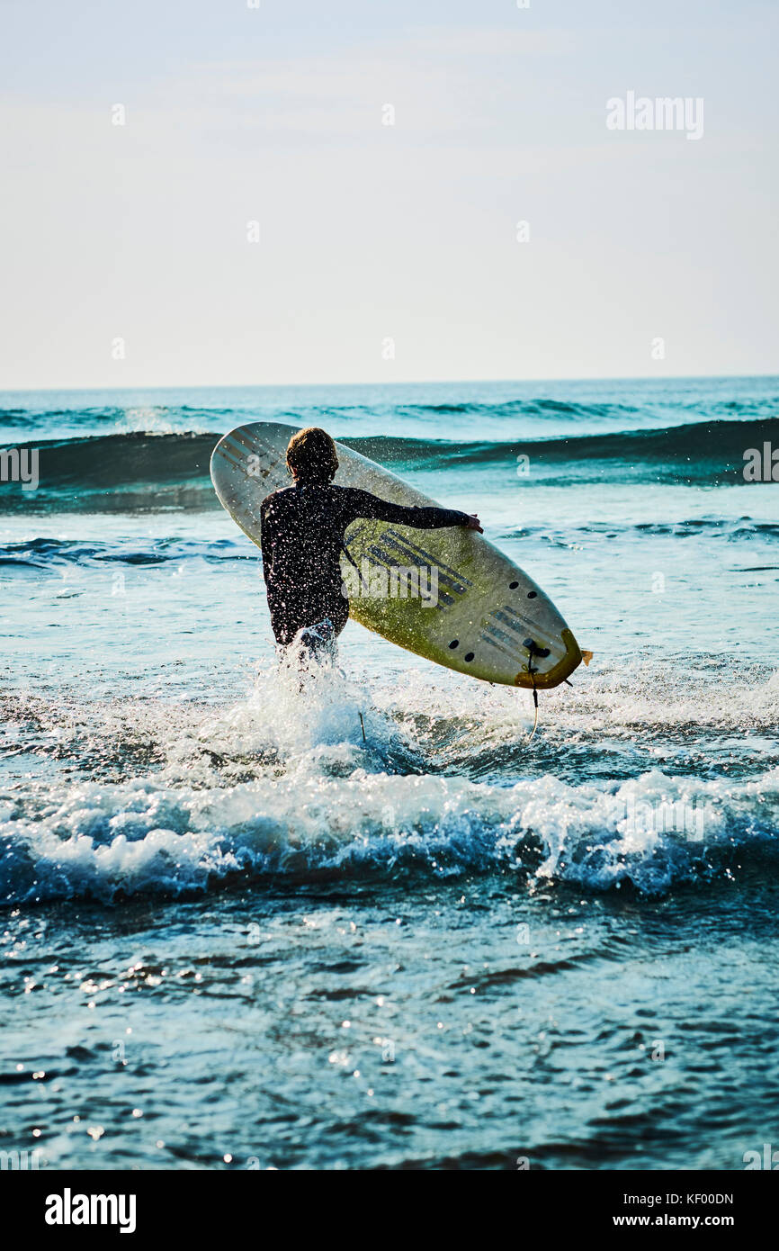 A young boy surfer with his surfboard running out to catch the waves. Stock Photo
