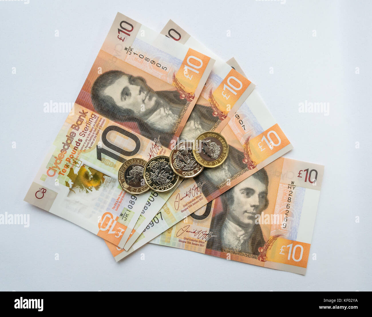 Plastic polymer Clydesdale Bank Scottish ten pounds £10 banknotes with Robert Burns and hexagonal one pound £1 coins on a plain white background Stock Photo