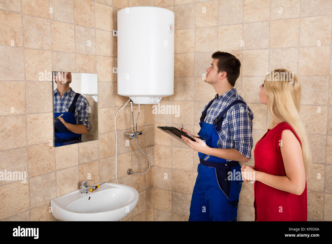Woman Looking At Young Male Plumber Holding Clipboard Looking At Electric Boiler Stock Photo