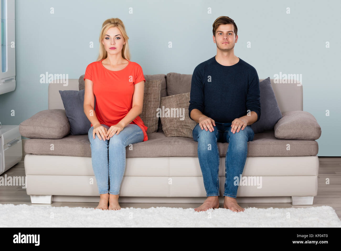Portrait Of Young Shy Couple Sitting On Sofa At Home Stock Photo