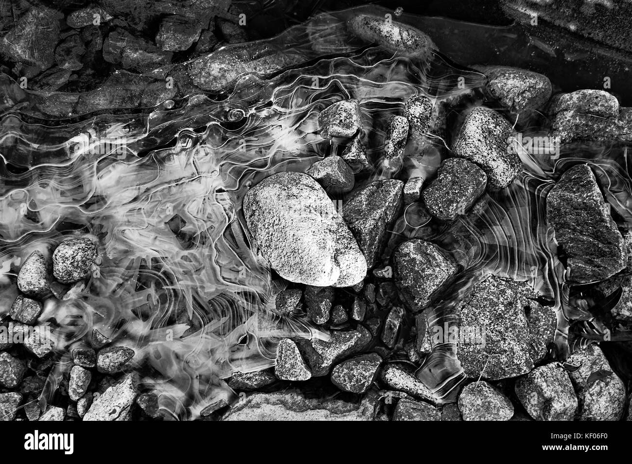 Ice trapped washed boulders of Snow river riverbed during winter cold with frost pattern on frozen water in NSW, Australia converted to black-white. Stock Photo