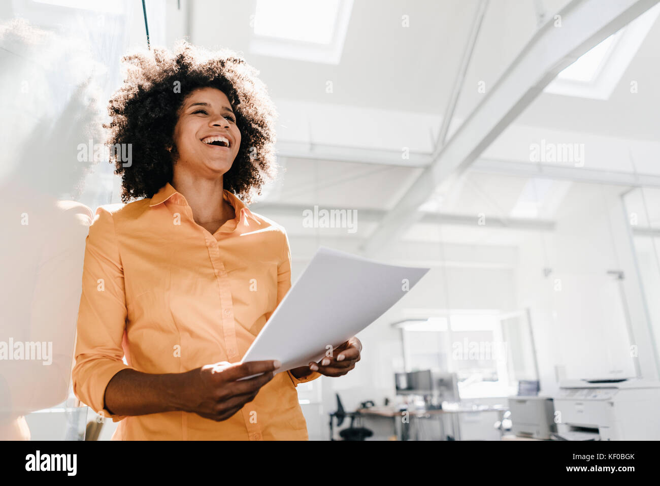 Laughing young woman holding documents in office Stock Photo - Alamy