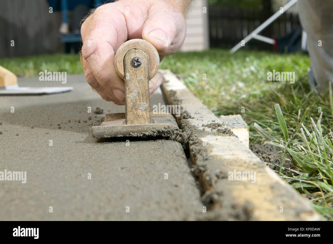 A close up of a man using a concrete edging tool on wet cement slab with timber form work Stock