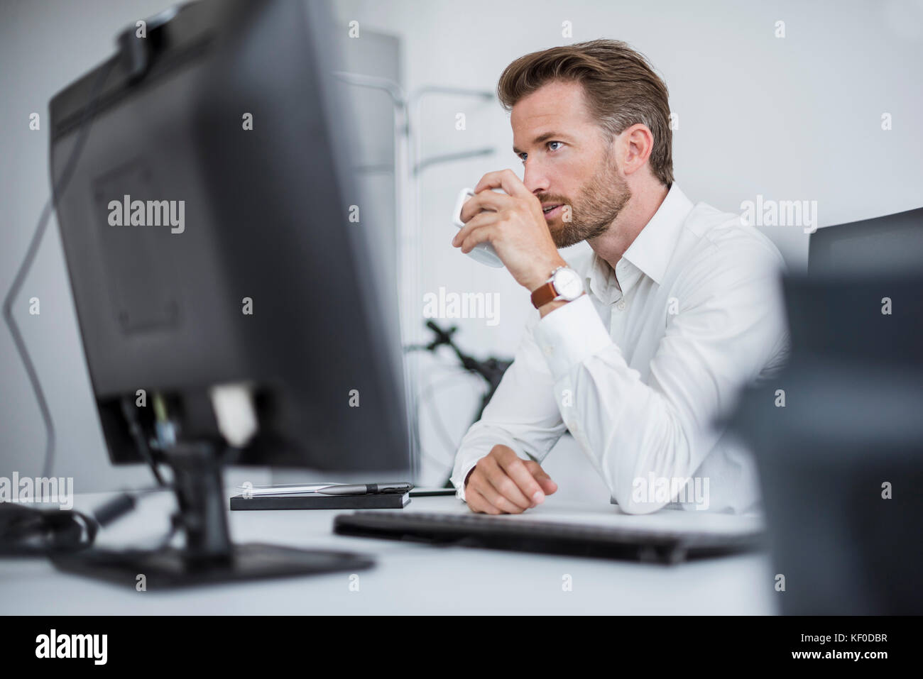 Portrait of serious businessman sitting at desk in the office drinking coffee Stock Photo