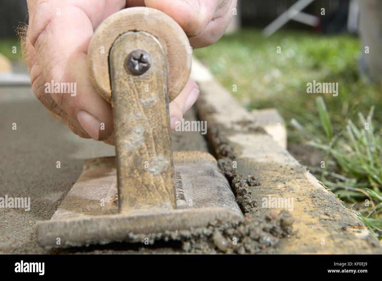A close up of a man using a concrete edging tool on wet cement slab with timber form work Stock