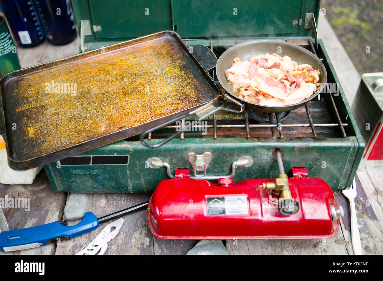 Bacon cooks and sizzles in a frying pan on a gas camping stove Stock