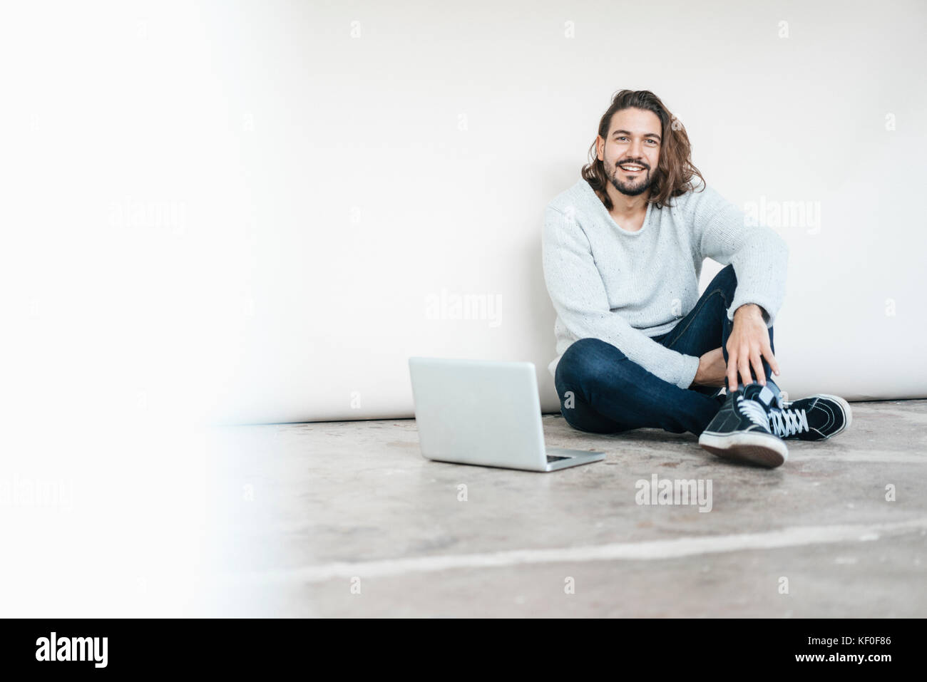 Portrait of smiling man with laptop sitting on the floor Stock Photo ...
