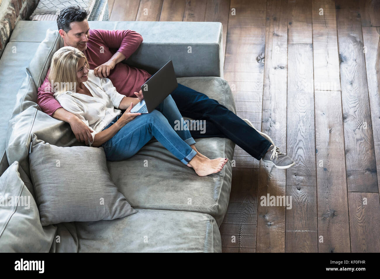Couple sitting on couch, using laptop Stock Photo - Alamy