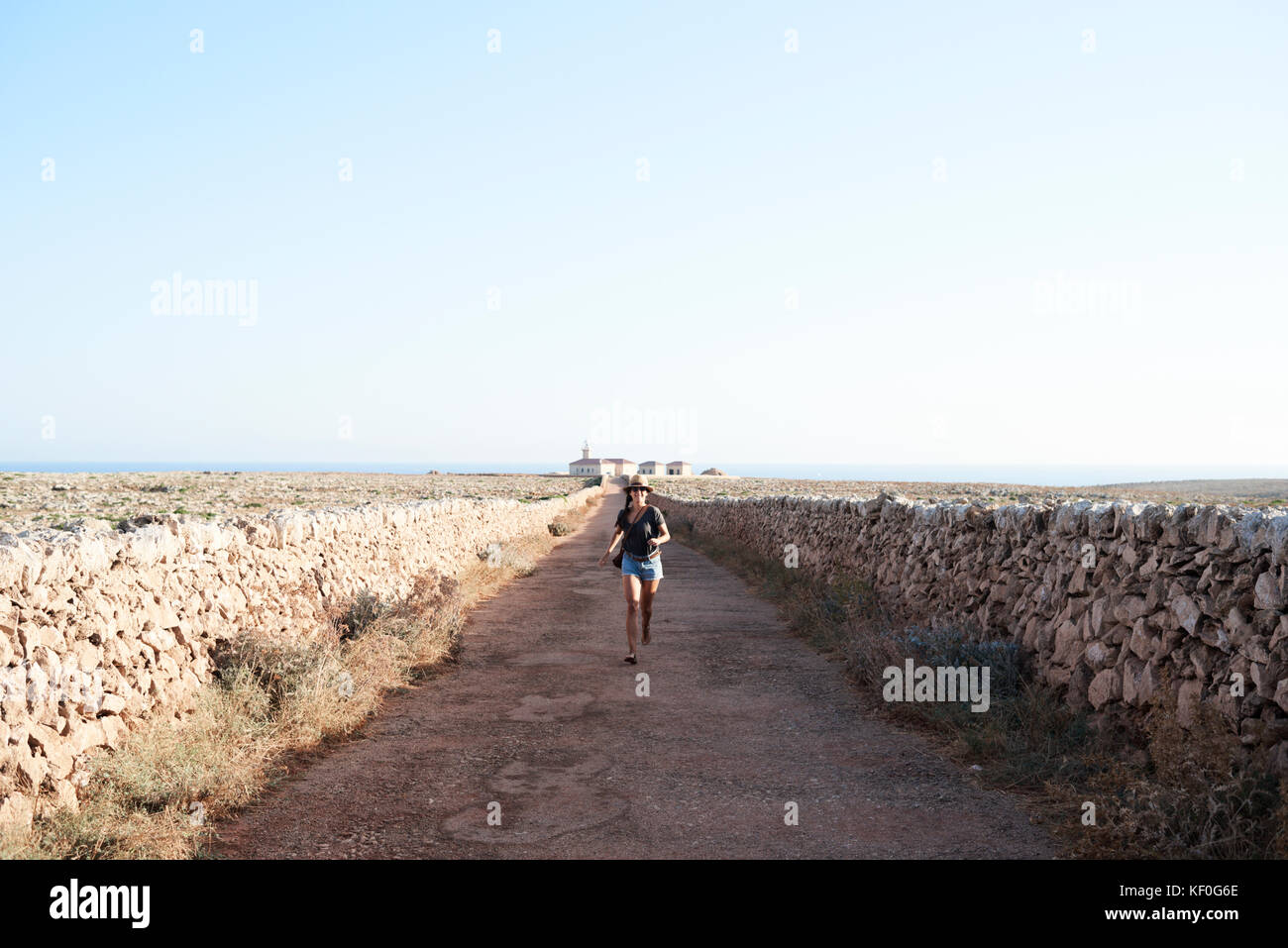 Menorca, Spain, happy solo traveler running in a empty road to a lighthouse in Menorca island, solo traveler Stock Photo