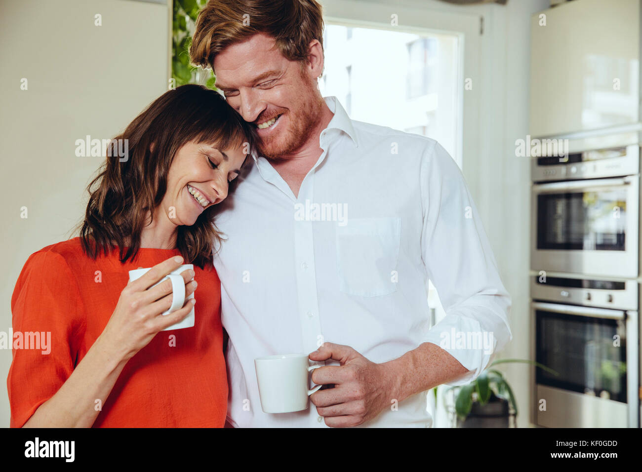 Happy couple in kitchen holding coffee mugs Stock Photo