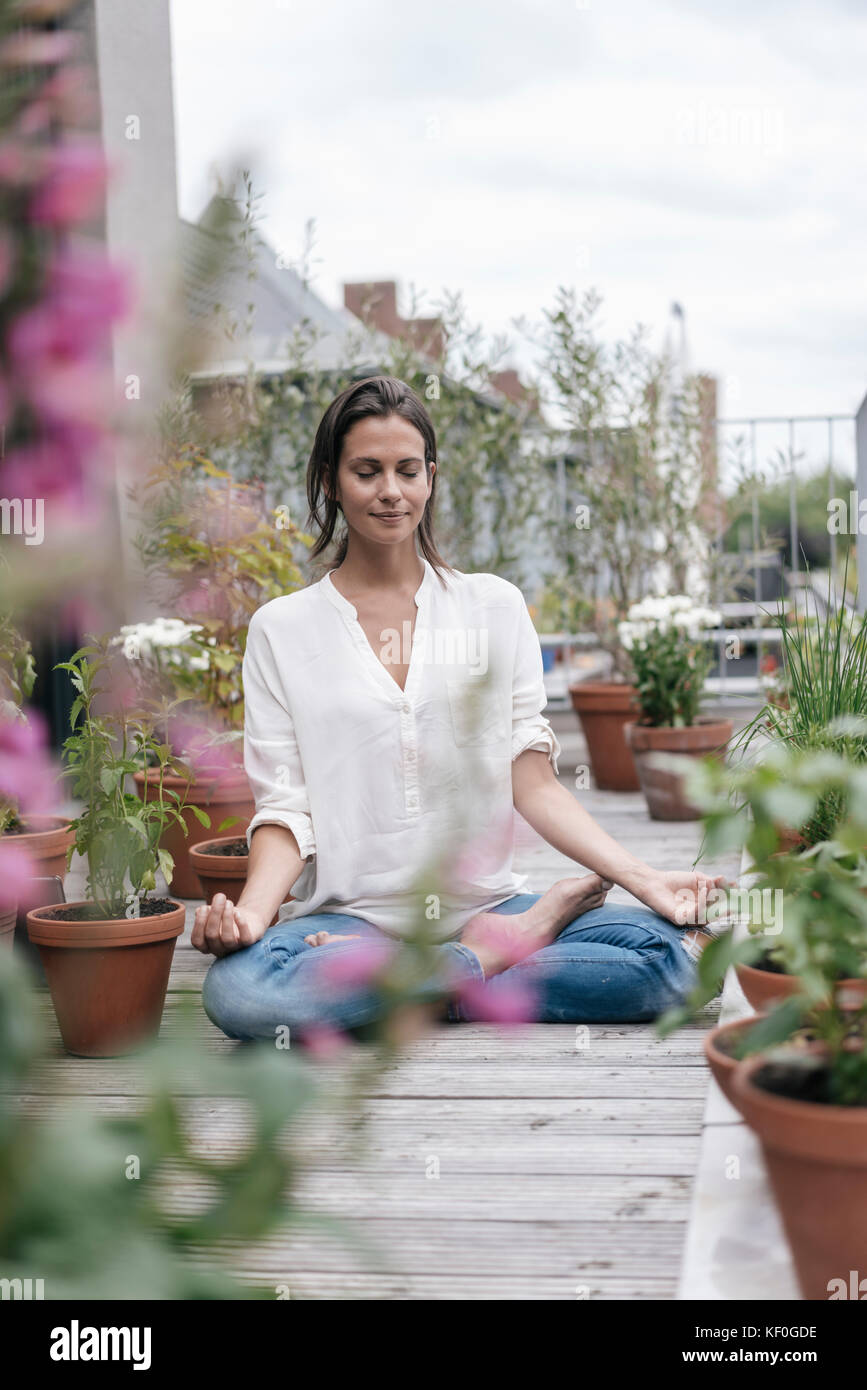 Woman sitting on balcony practicing yoga Stock Photo