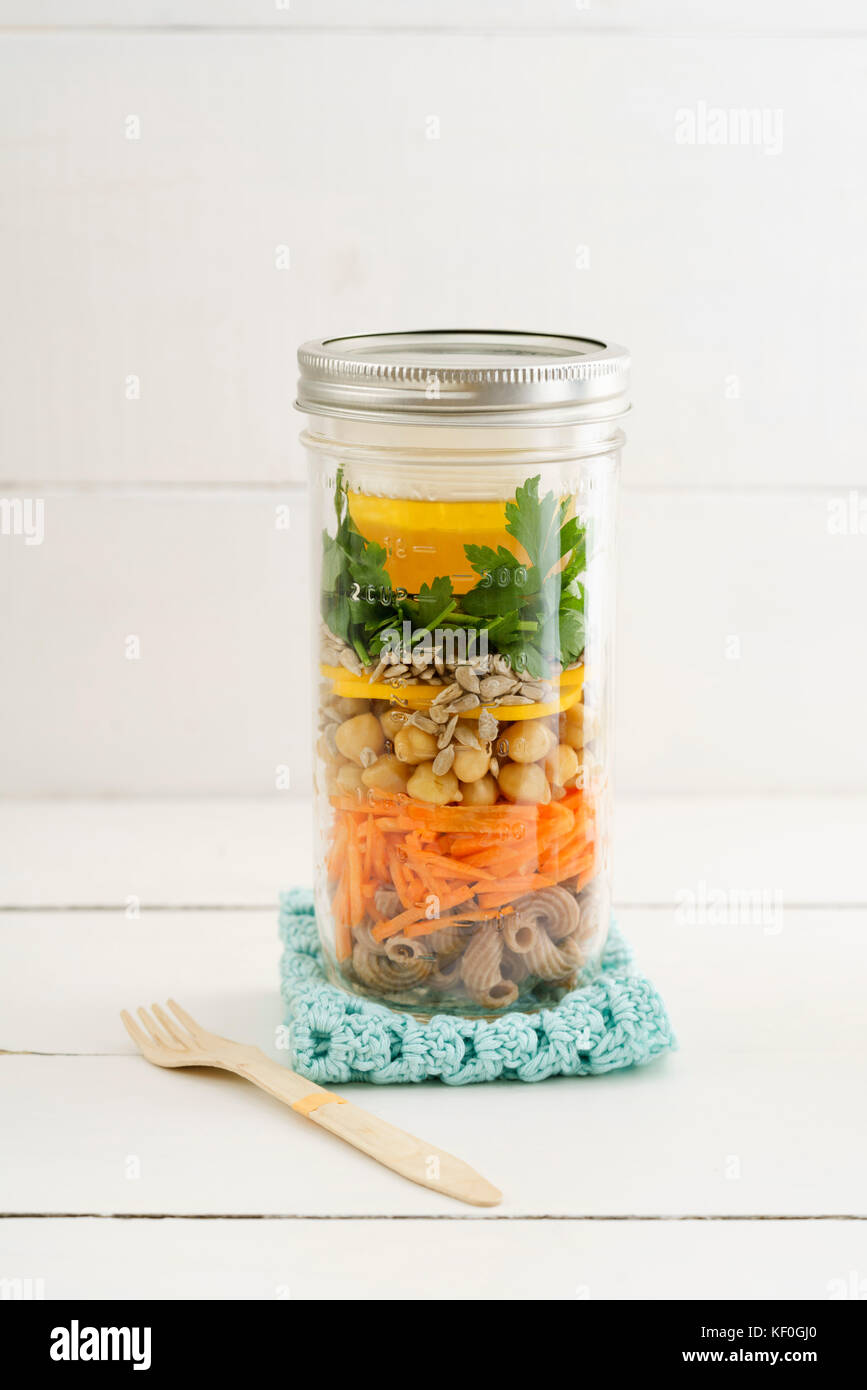 Vegan and vegetarian salad to go in a jar with whole grain pasta, carrots, chickpeas, yellow zucchini, sunflower seeds, parsley and vinaigrette on woo Stock Photo