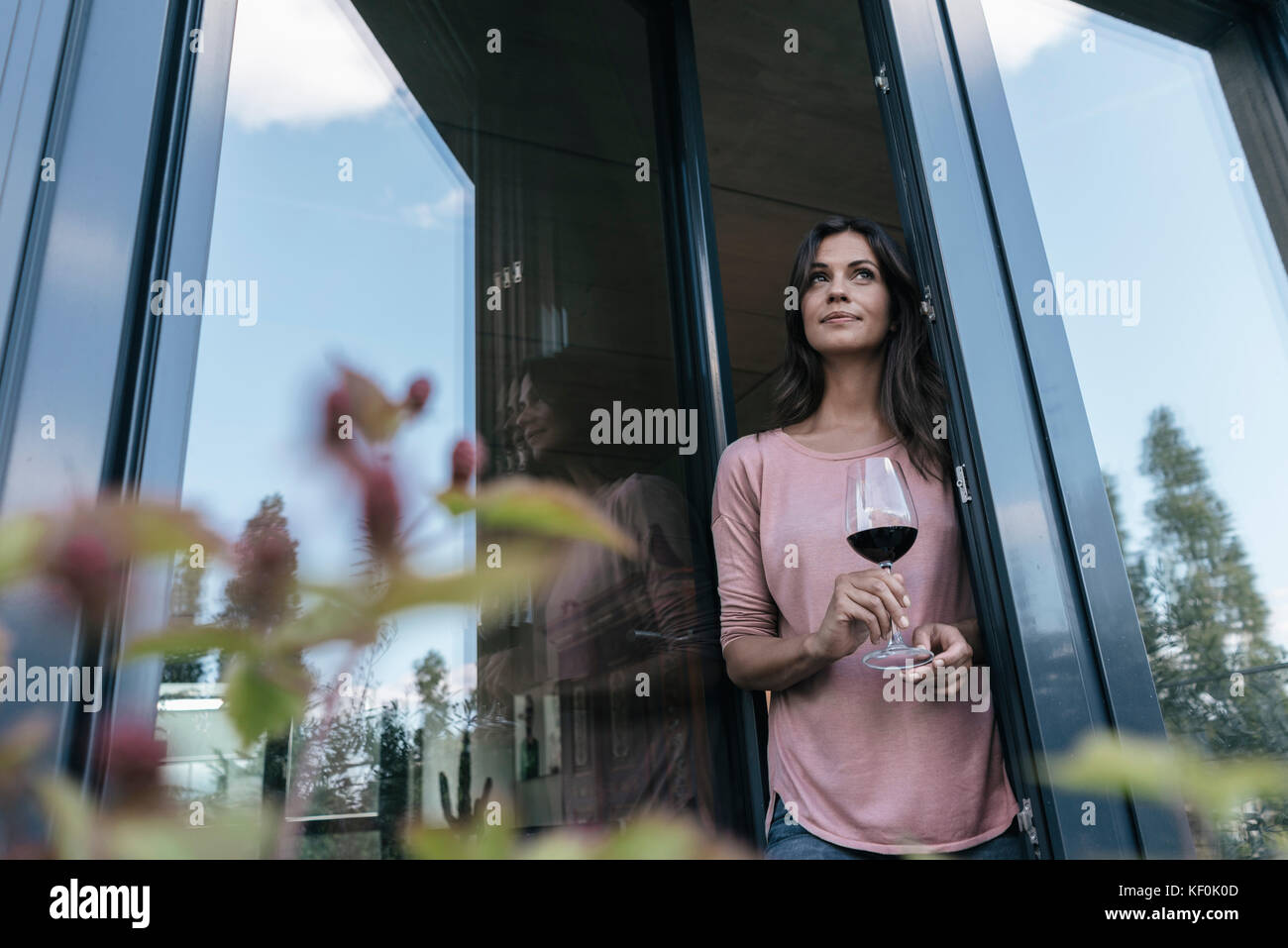 Woman holding glass of red wine looking out of window Stock Photo - Alamy