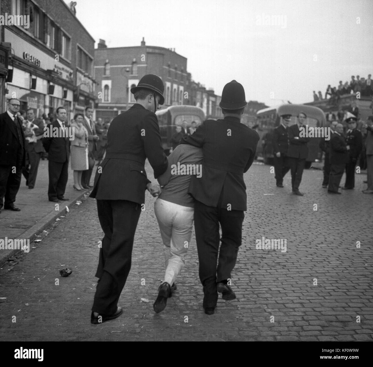 Firmly grasped by two police officers, a man is removed from the meeting of Sir Oswald Mosley's Union Movement at Ridley Road, Dalston, London. the hostile crowd shouted and booed as Sir Oswald tried to speak, and after five minutes he ended the meeting on police advice. Stock Photo