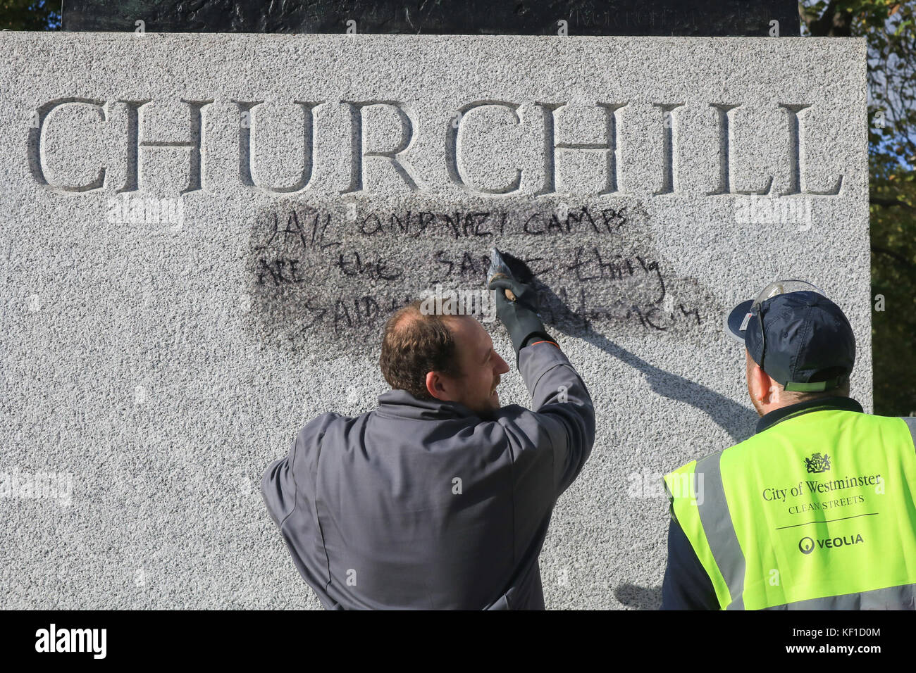 London, UK. 25th Oct, 2017. Westminster council Anti Graffiti unit wash and clean the Graffiti with the writing  still legible  ''Jail and Nazi camps are the same thing'  on the statue of Sir Winston Churchill opposite the Palace of Westminster left by Calais Jungle protesters the previous day. Credit: amer ghazzal/Alamy Live News Stock Photo